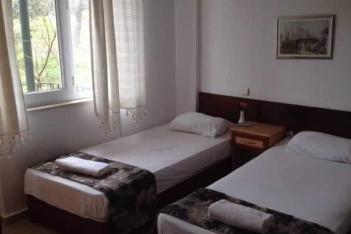 A hotel room with two single beds, a nightstand with a lamp, and a window with curtains.