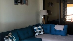 A living room with a blue sofa, a round coffee table, and a 'HAPPY' sign on the wall. - 47m2 duplex apartment - type 2 with terrace (Frejus)