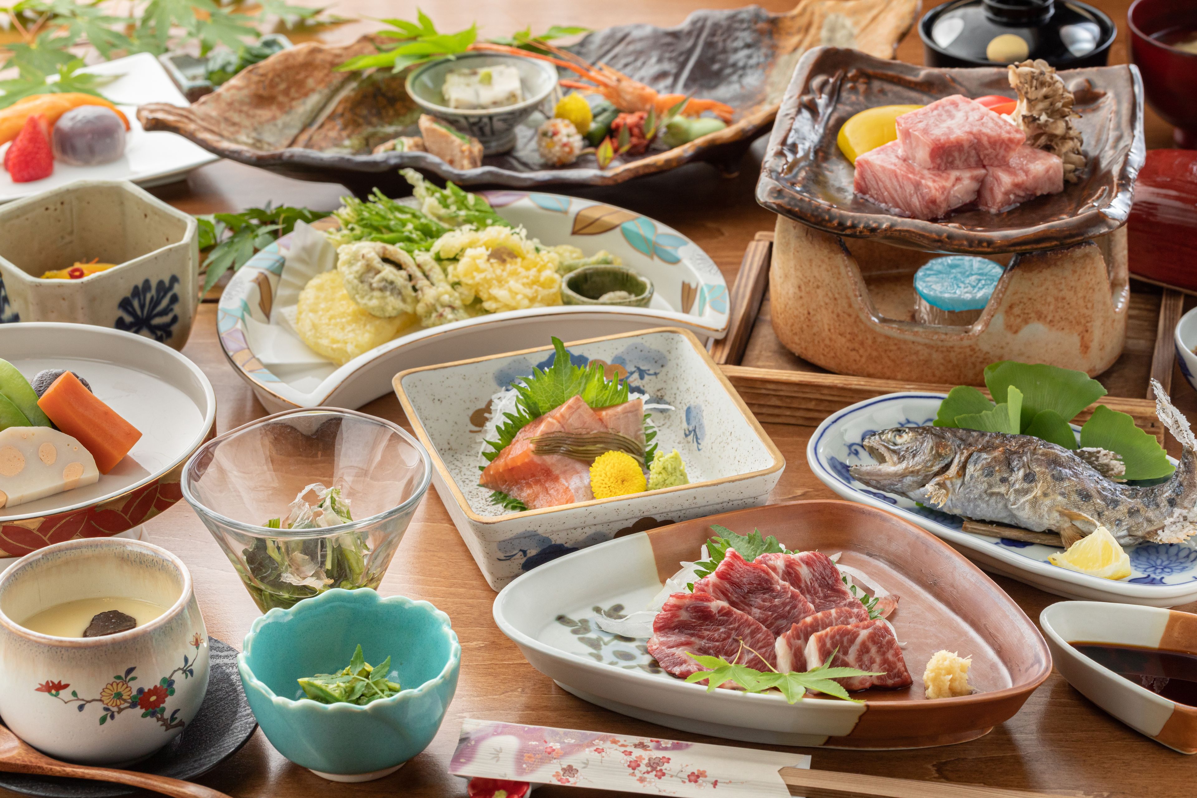 Une variété de plats japonais présentés sur une table en bois, notamment des sushis, des sashimis et d’autres plats traditionnels.