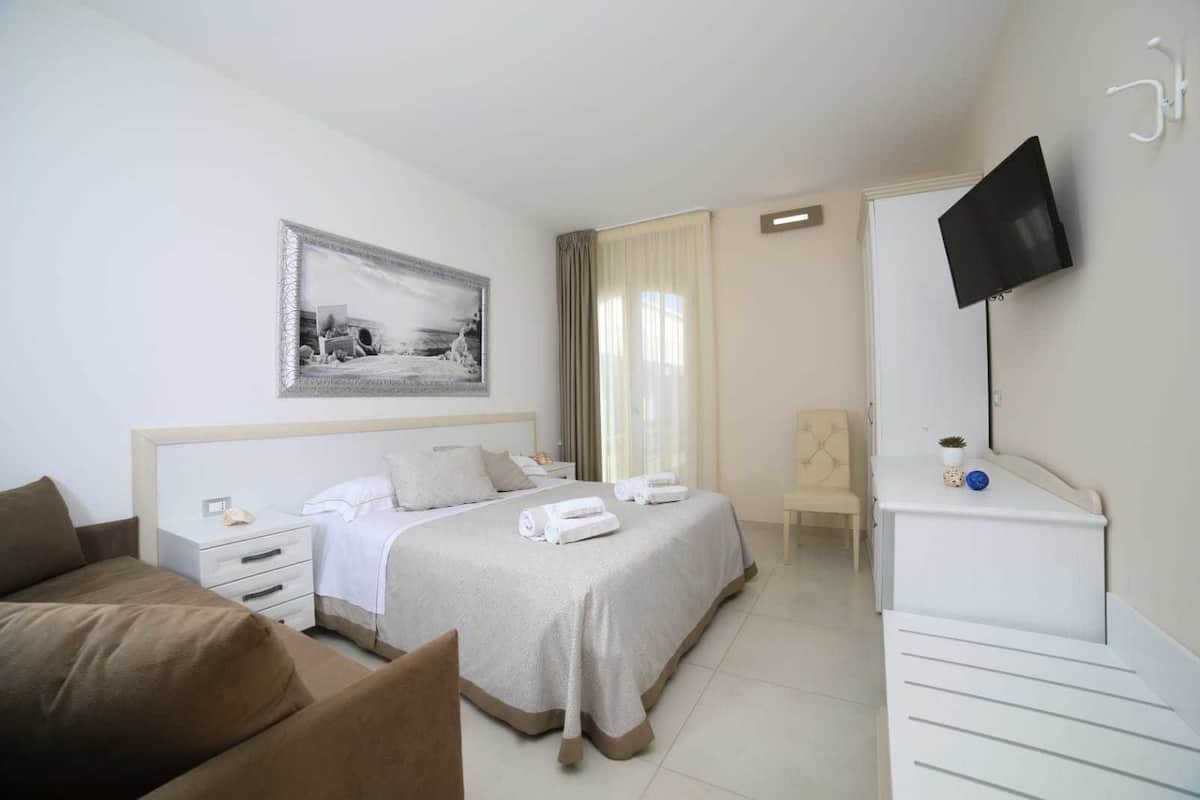 A hotel room with a bed, a desk, a chair, a television, and a painting on the wall.