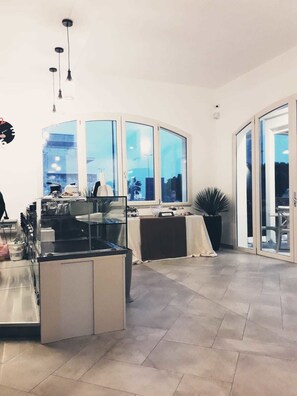 A modern kitchen with a glass partition, a dining area with a table and chairs, and large windows with a city view. - Bella Costa (Porto Cesareo)