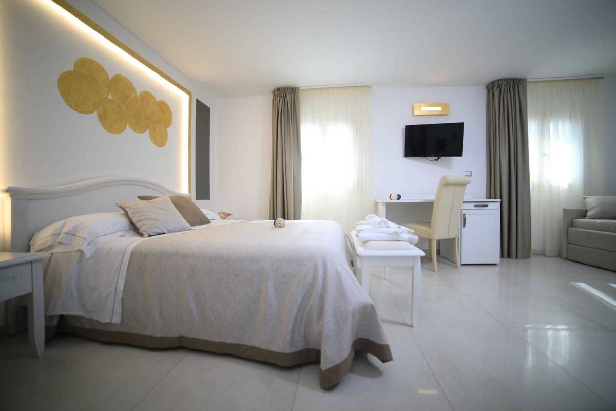 A modern hotel room with a large bed, a desk, a chair, and a TV.