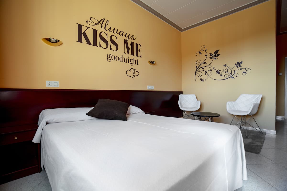 A hotel room with a large bed, two white chairs, and a wall with a decorative sign.