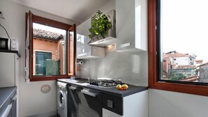 A compact kitchen with a washing machine, a stove, and a window overlooking a residential area. - Grimaldi Apartments - Ca Sole (Venice)