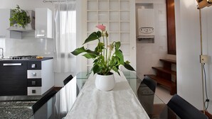 A modern kitchen with a dining area, featuring a white table, chairs, and a potted plant with a pink flower. - Grimaldi Apartments - Ca Sole (Venice)