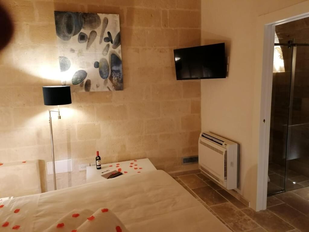 A hotel room with a bed, a flat-screen TV mounted on the wall, a radiator, and a glass shower enclosure.