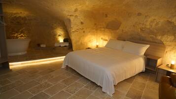 A bedroom with a stone wall, a bed, a bathtub, and a nightstand with a lamp.