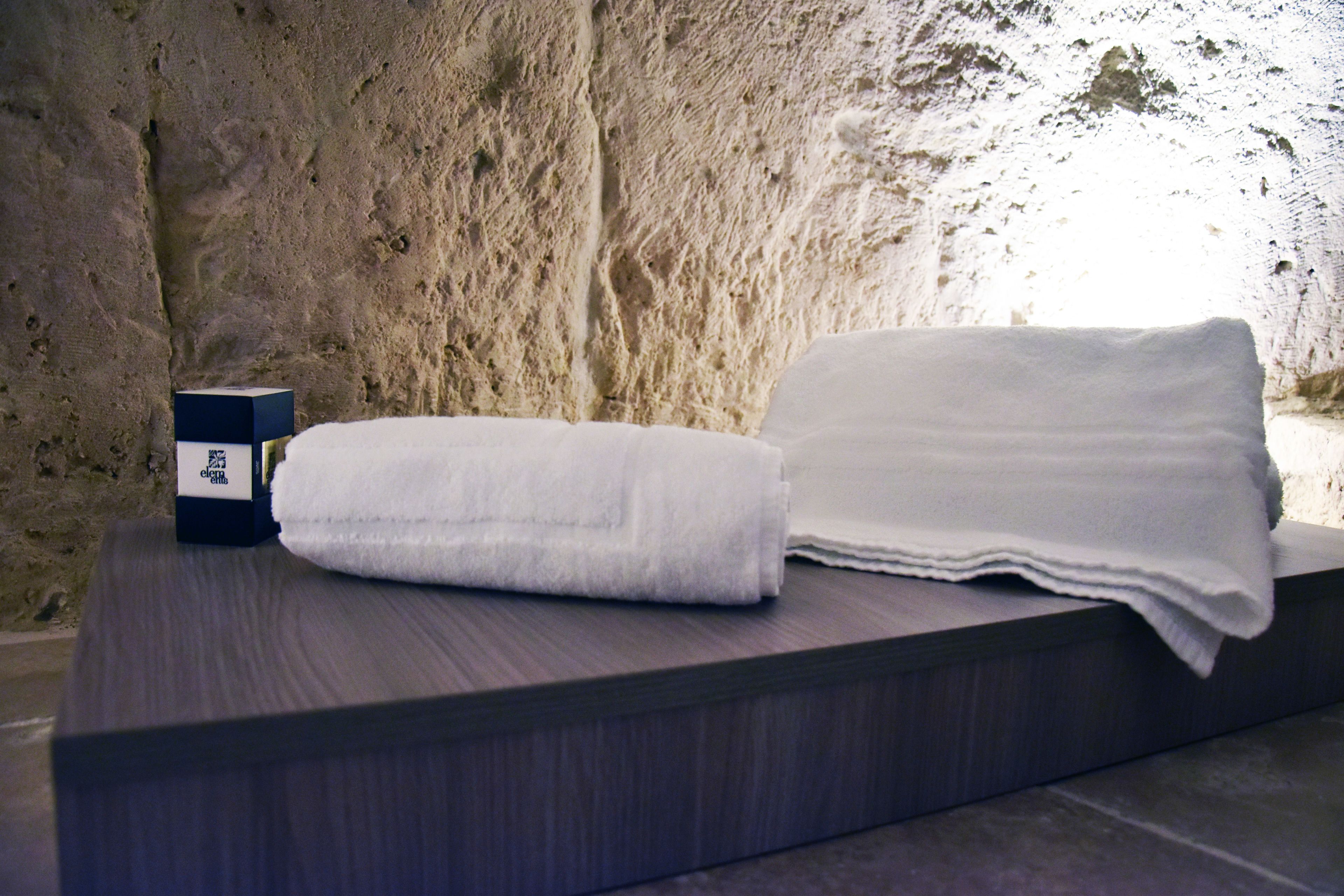 A neatly folded white towel and a box on a dark wooden surface against a textured stone wall.