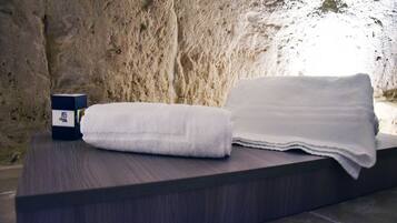 Una toalla blanca doblada con cuidado y una caja sobre una superficie de madera oscura, frente a una pared de piedra con textura.