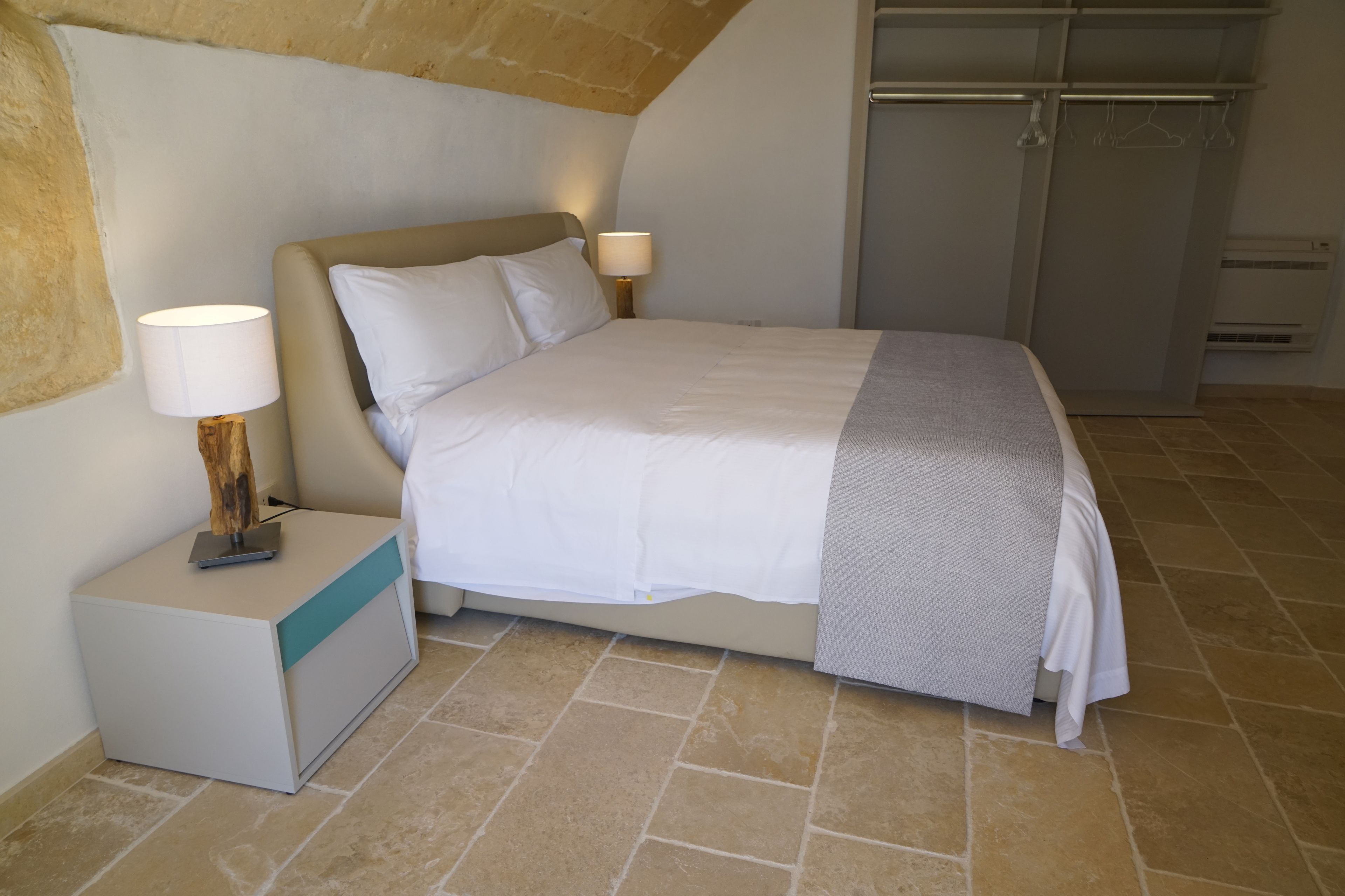 Um quarto com cama, mesas de cabeceira, abajur e guarda-roupa.