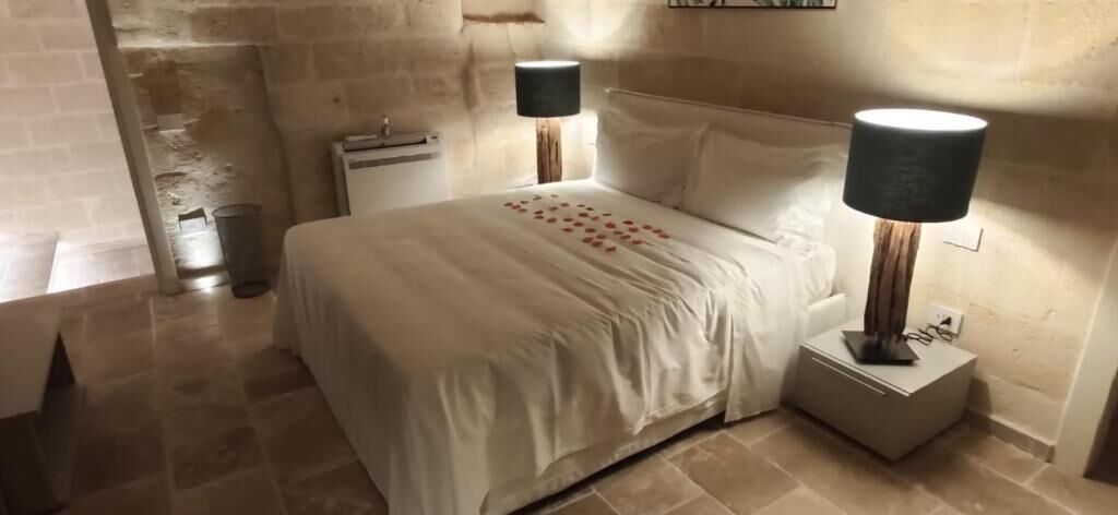 A bedroom with a bed, two bedside lamps, a nightstand, and a tiled floor.