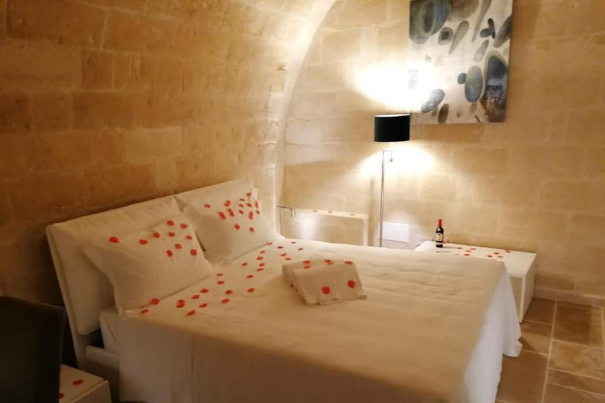 A bedroom with a large bed, a bedside table, a nightstand, and a wall-mounted lamp.