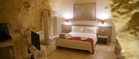 A hotel room with a stone arch, a bed with white linens, a flat-screen TV, a bedside table, and a lamp.