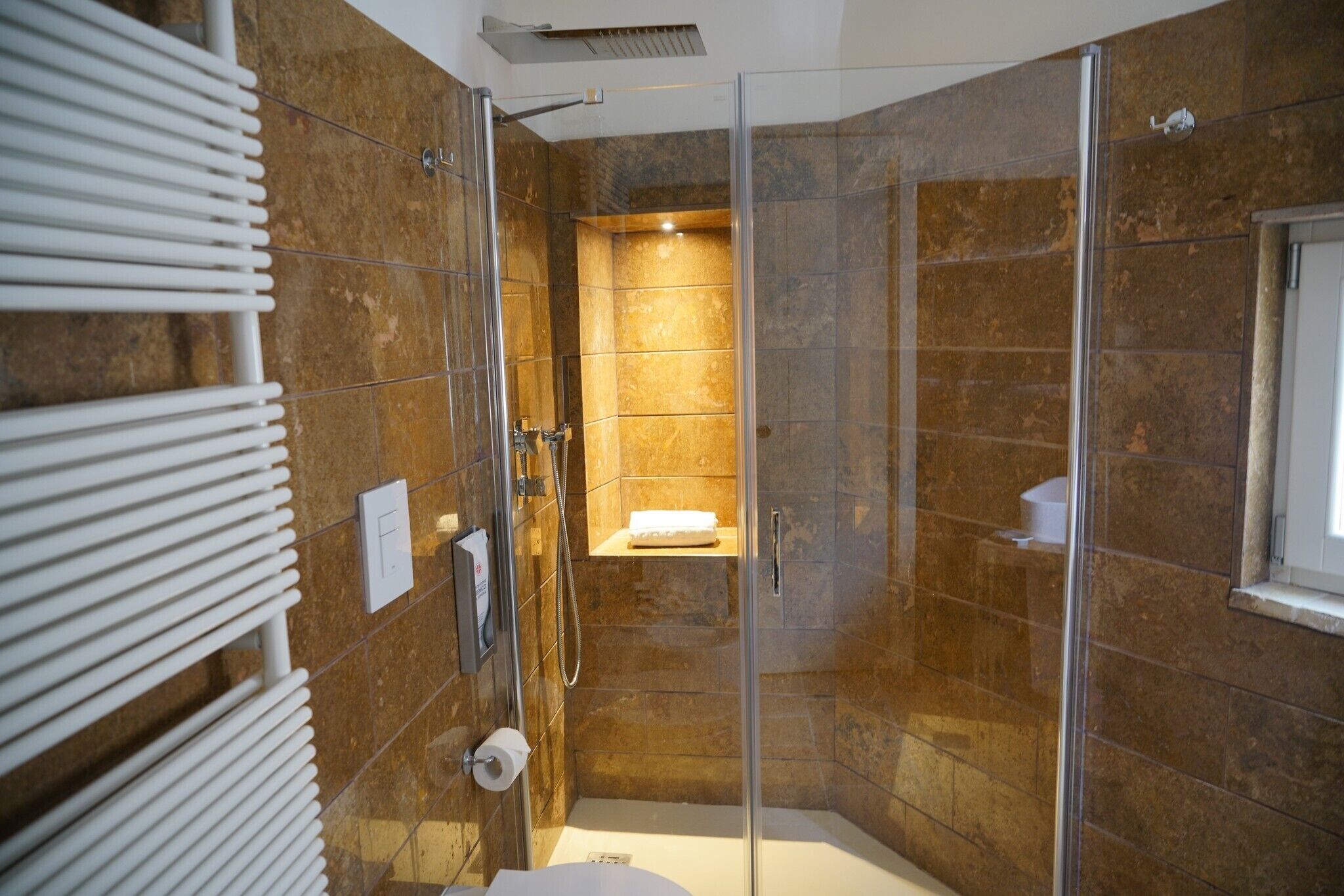 A modern bathroom with a glass-enclosed shower, a white towel rack, and a toilet.