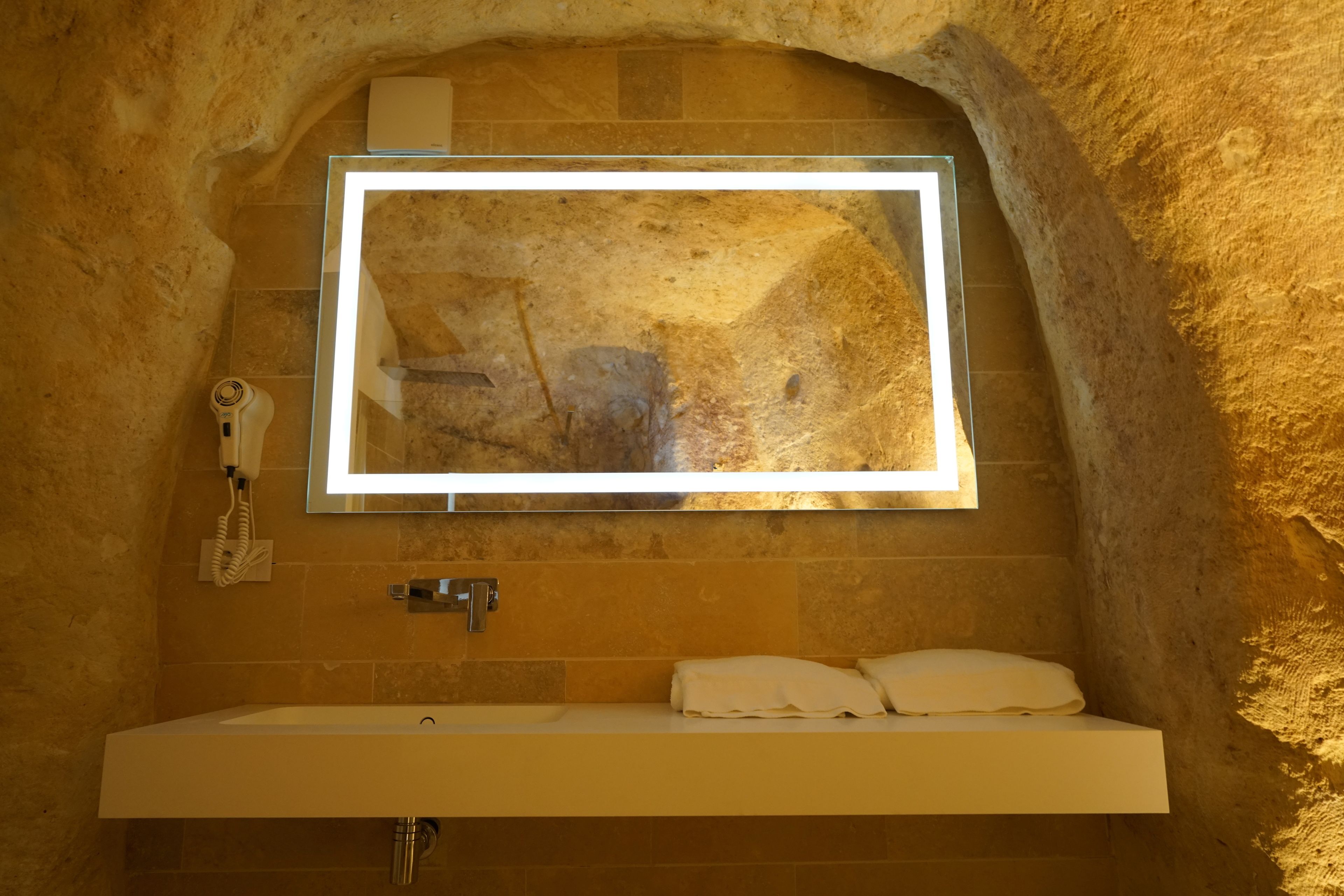 A bathroom with a stone wall, a mirror, a sink, and a towel rack.