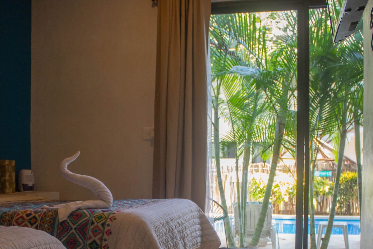 A hotel room with two beds, a view of palm trees and a pool through a glass door.