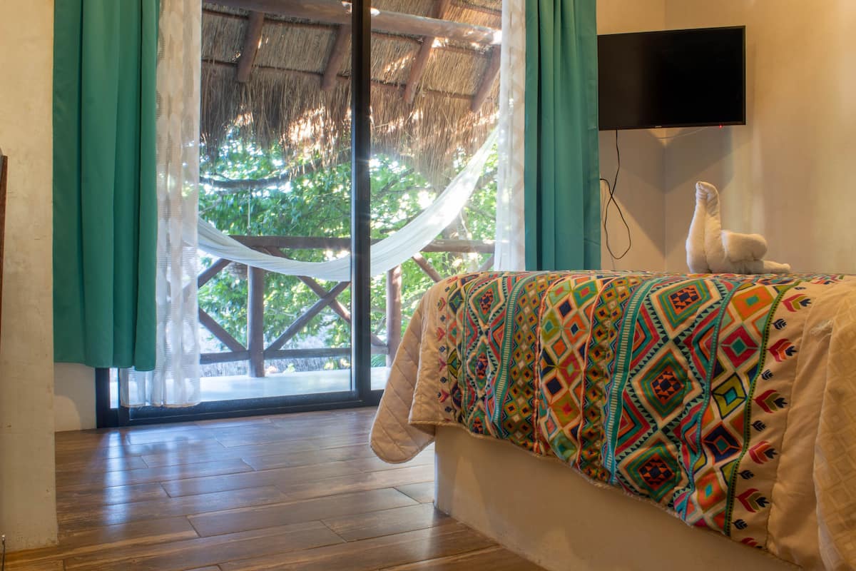 A room with a bed, a TV mounted on the wall, and a view of greenery outside.