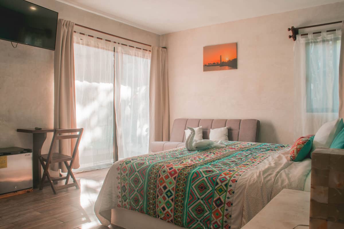 A bedroom with a bed, a chair, a desk, and a TV.