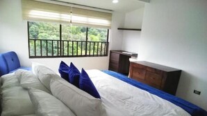A bedroom with a bed, a dresser, and a window with a view of greenery. - Casa Grande Exclusiva Zona Norte (Armenia)