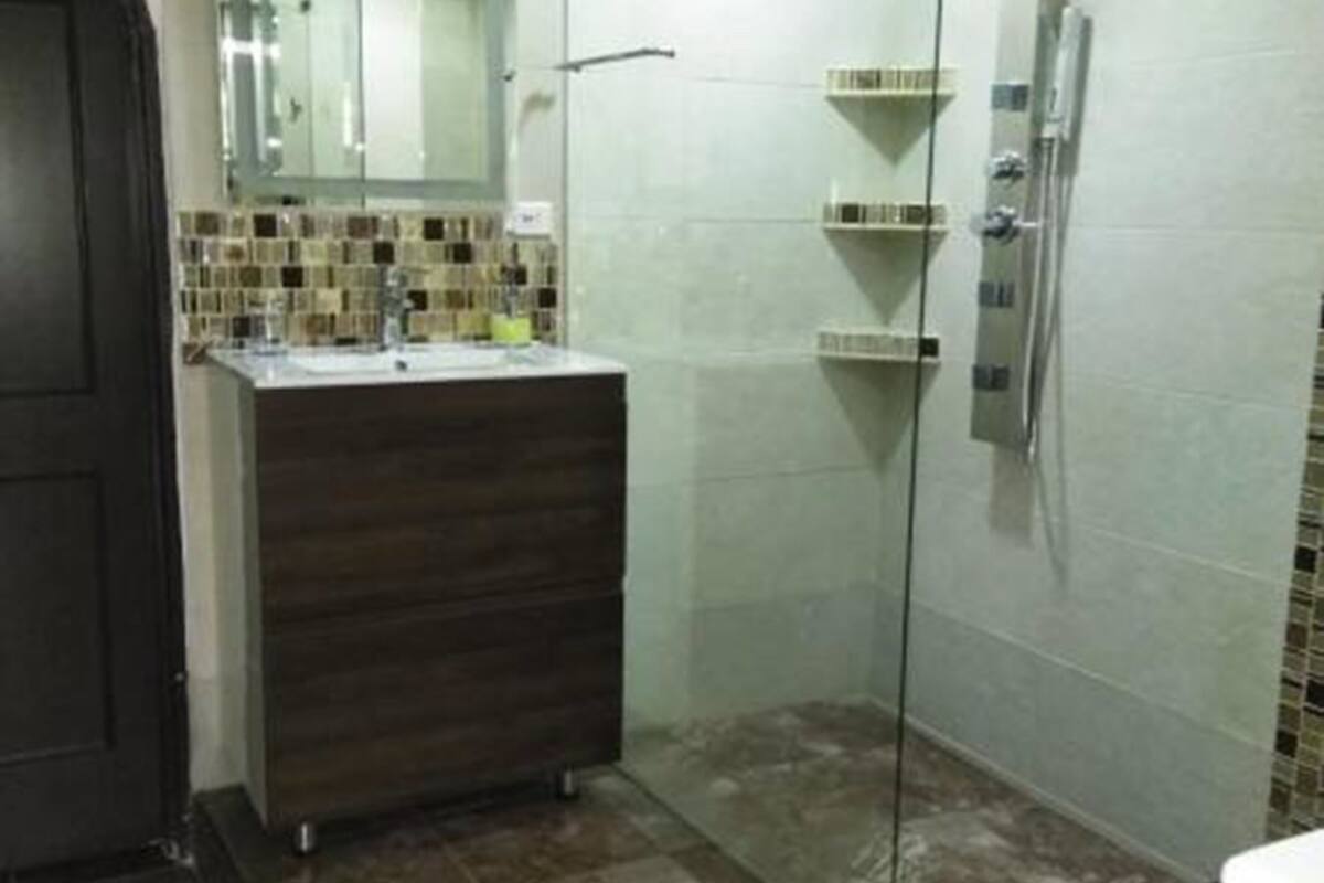 A bathroom with a glass shower enclosure, a dark wooden vanity, and a tiled floor.