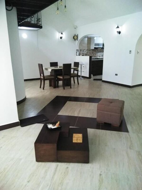 A spacious living area with a dining table and chairs, a kitchen in the background, and a unique black and white floor design.