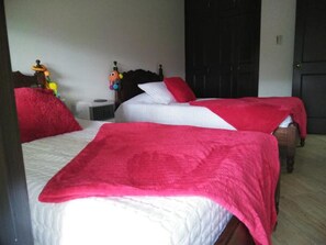 Una habitación con dos camas, cada una con una manta roja y ropa de cama blanca. Hay una mesita con una lámpara y un juguete encima.