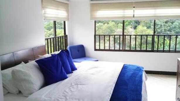A bedroom with a bed, a chair, a wardrobe, and a balcony with a view of greenery. - Casa Grande Exclusiva Zona Norte (Armenia)