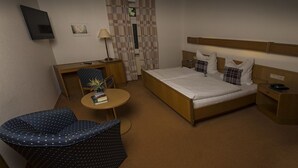 A hotel room with a bed, a desk, a chair, a small table, and a TV.