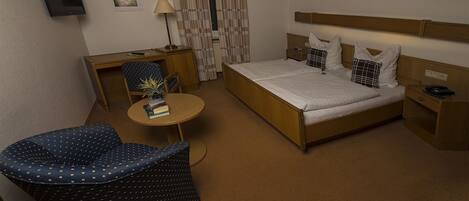 Una habitación de hotel con cama, escritorio, silla, mesita y televisor.