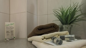A bathroom with a towel rack holding a brown towel, a white towel, and a bottle of hand soap. There is a potted plant on the counter and a sign with text.