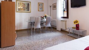 Une chambre d’hôtel comprenant un lit, une table à manger avec des chaises, un téléviseur fixé au mur et deux tableaux encadrés accrochés au mur.