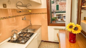 Une cuisine équipée d’une cuisinière à gaz, d’un évier et d’une fenêtre donnant sur un immeuble.
