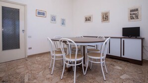 Un'area pranzo con un tavolo rotondo, quattro sedie, un televisore su un mobile e quadri appesi al muro.