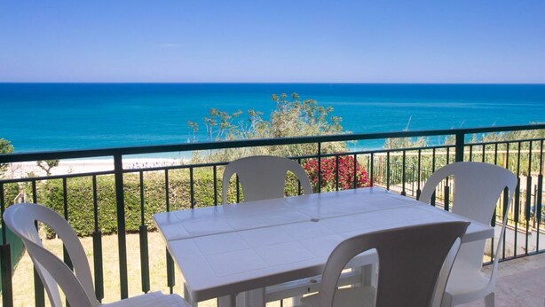 Un balcon avec une table et des chaises donnant sur une plage.