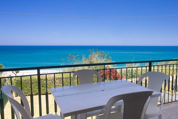 A balcony with a table and chairs overlooking a beach.