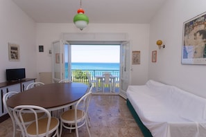 Une piÚce comprenant une table à manger, des chaises, un canapé, un téléviseur et un balcon avec vue sur la mer.