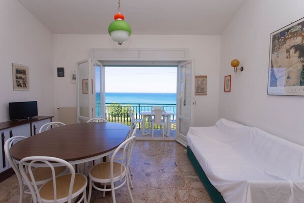 Une piÚce comprenant une table à manger, des chaises, un canapé, un téléviseur et un balcon avec vue sur la mer.