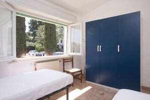 A bedroom with a bed, a chair, a window, and a blue wardrobe.