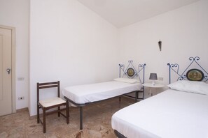 Une chambre avec deux lits, une chaise, une petite table avec une lampe et un luminaire fixé au mur.