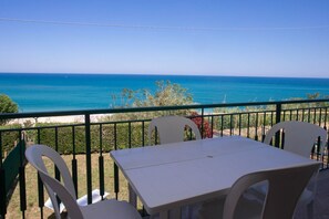 A balcony with a table and chairs overlooking a beach and ocean.