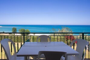 A balcony with a table and chairs, overlooking a clear blue sea and distant land.