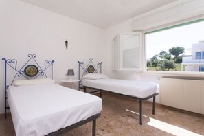 Une chambre avec deux lits, une fenĂȘtre, un radiateur et un luminaire fixĂ© au mur.