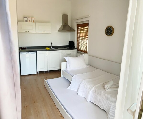 A compact room with a bed, a kitchenette, and a window with blinds.