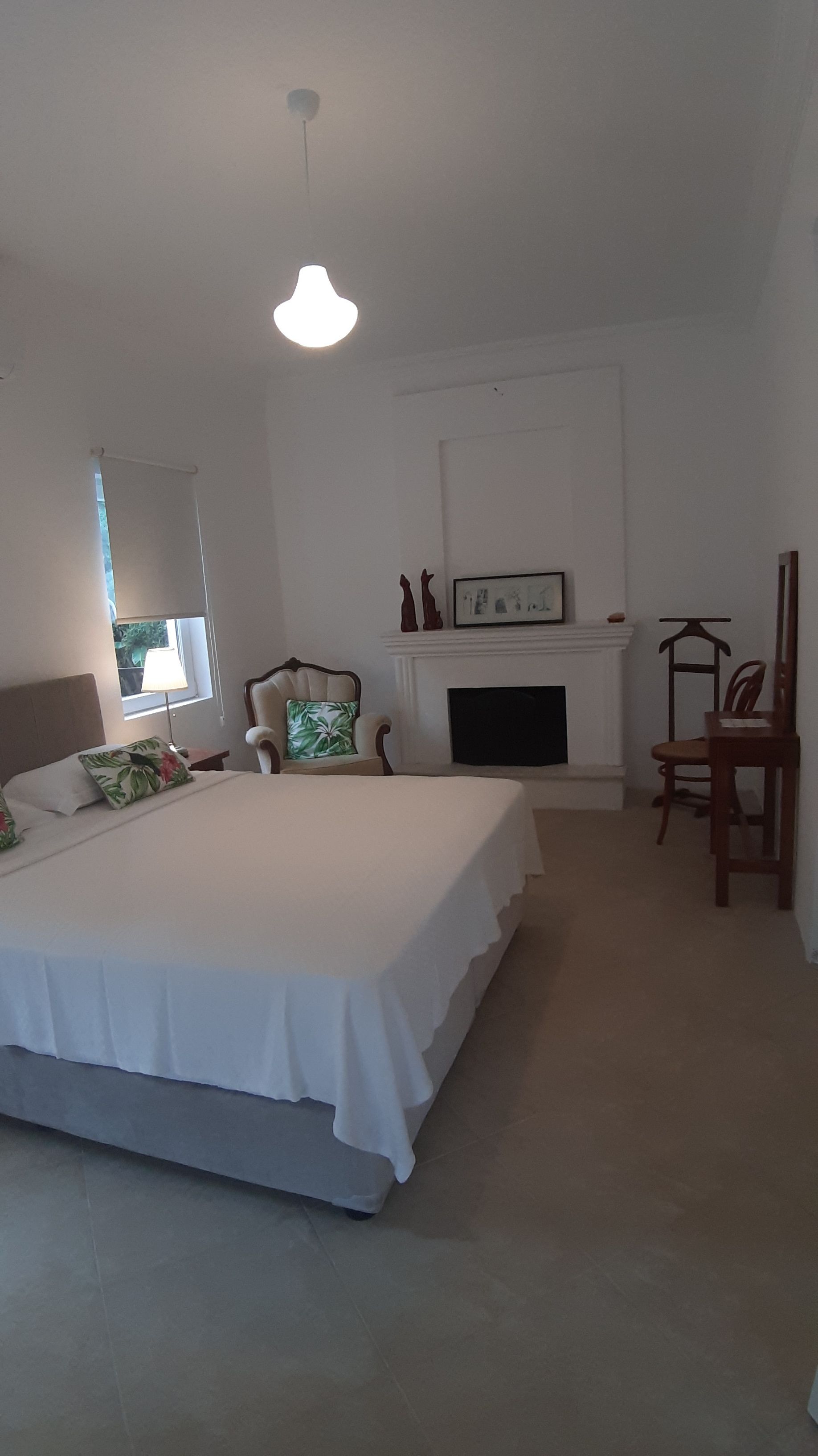 Un dormitorio con una cama grande, una silla, una chimenea y un colgador de luz.