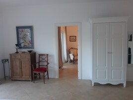 Una habitación con un armario de madera, una silla con cojín rojo, un guardarropa blanco y un cuadro en la pared.