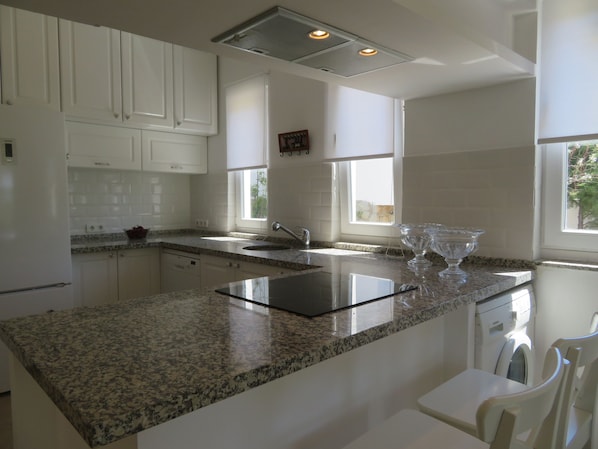 Una cocina moderna con armarios blancos, encimeras de granito, un lavamanos de acero inoxidable y un lavavajillas integrado.