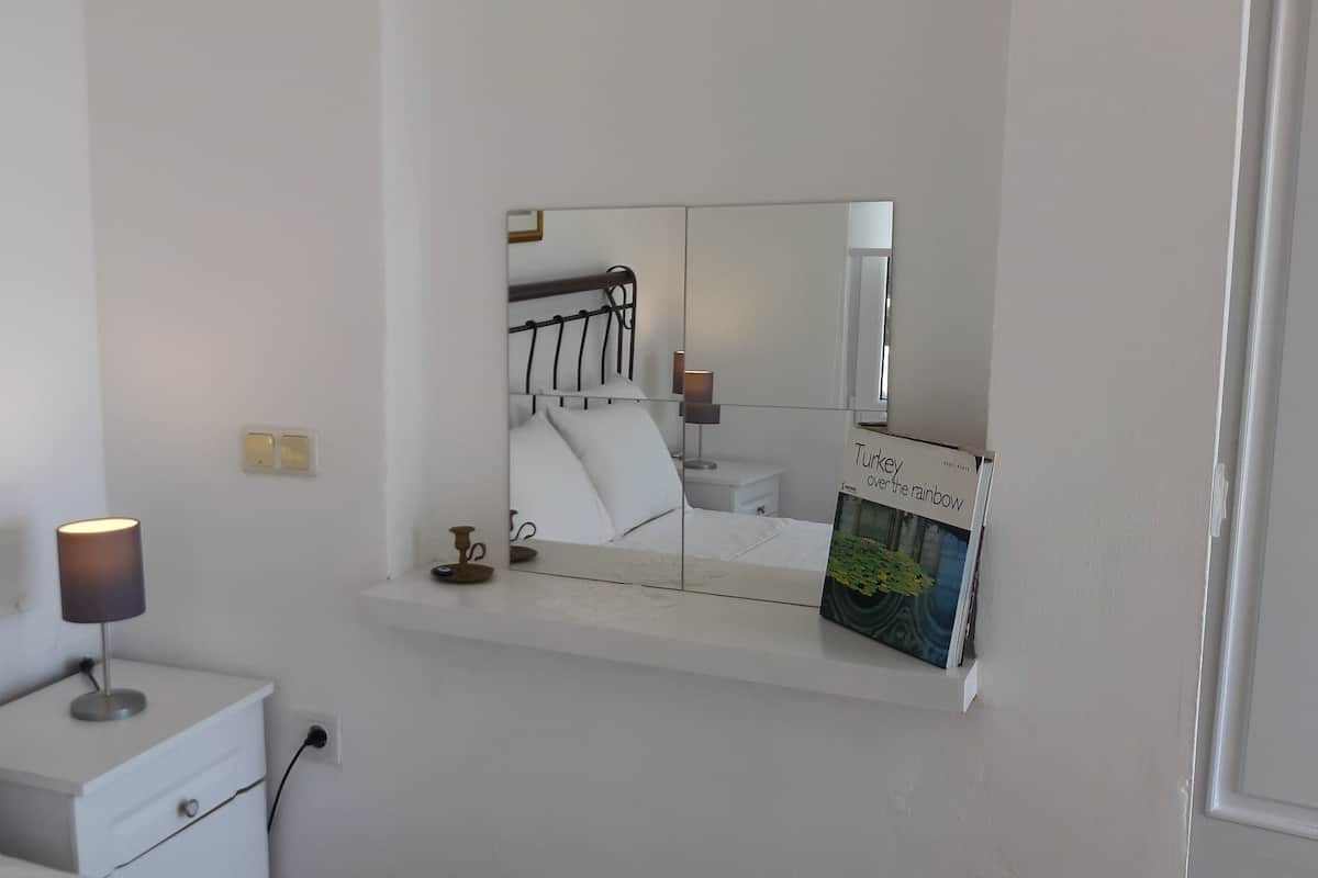 A bedroom with a bed, bedside table, lamp, nightstand, and a mirror reflecting the room.
