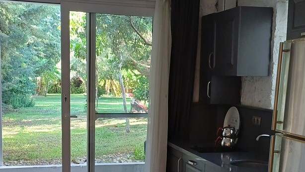 A kitchen with a washing machine, cabinets, and a view of a garden through a sliding door. - Villa White (Datça)