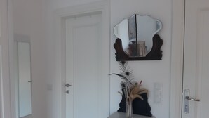 A white door with a mirror above it, a small black cabinet with a vase and decorative items, and a light switch on the wall. - Villa White (Datça)