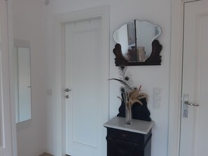 A white door with a mirror above it, a small black cabinet with a vase and decorative items, and a light switch on the wall. - Villa White (Datça)